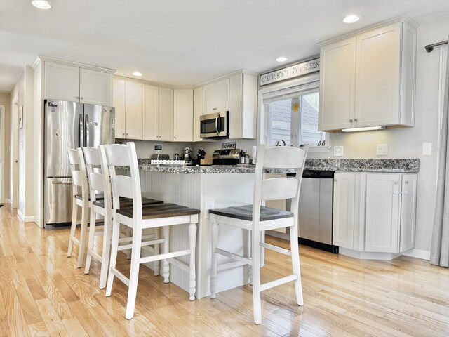 kitchen featuring light stone countertops, light hardwood / wood-style flooring, a breakfast bar, stainless steel appliances, and white cabinets