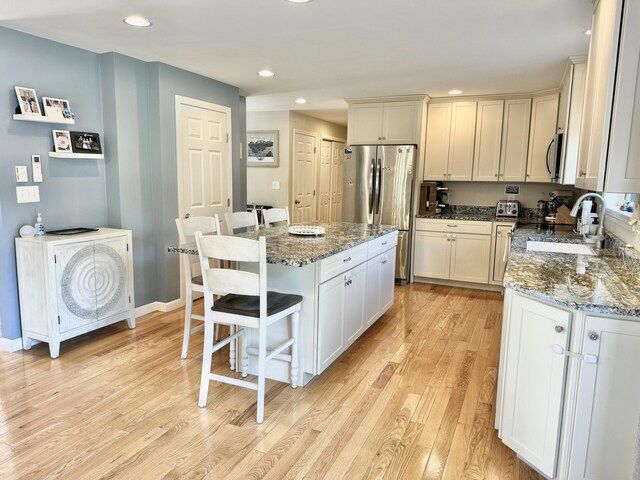 kitchen with dark stone countertops, light hardwood / wood-style flooring, a center island, appliances with stainless steel finishes, and a breakfast bar area