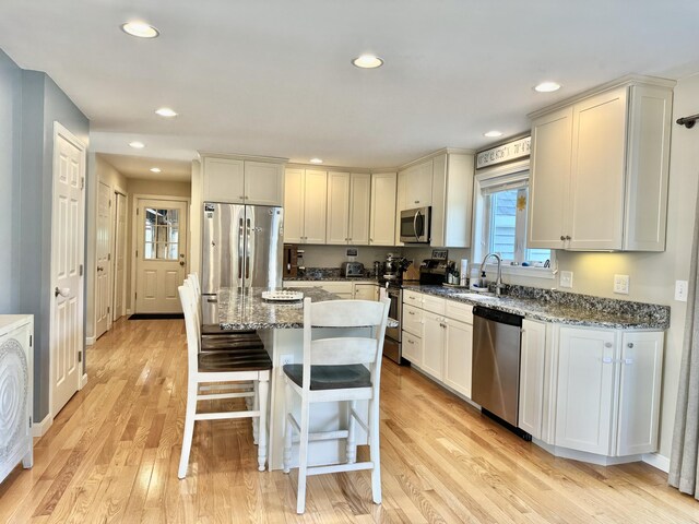 kitchen featuring a kitchen island, a kitchen breakfast bar, appliances with stainless steel finishes, light hardwood / wood-style floors, and light stone counters