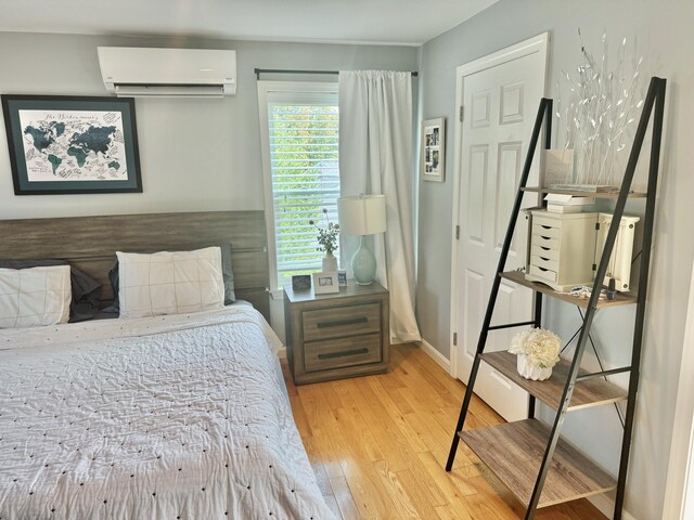 bedroom with a wall mounted AC and light hardwood / wood-style flooring