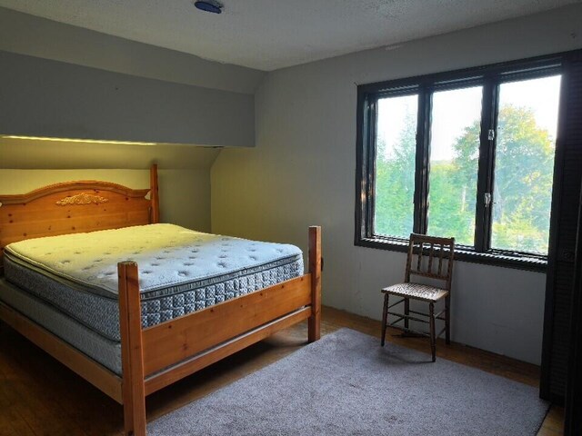 bedroom featuring hardwood / wood-style flooring, a textured ceiling, vaulted ceiling, and multiple windows