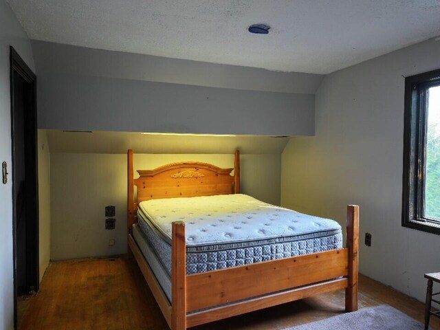 bedroom with vaulted ceiling, a textured ceiling, and dark wood-type flooring