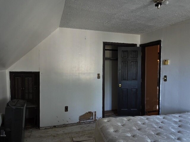 unfurnished bedroom featuring a textured ceiling, a closet, vaulted ceiling, and hardwood / wood-style flooring