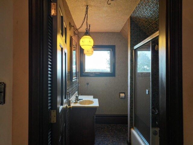 bathroom featuring shower / bath combination with glass door, vanity, and a textured ceiling