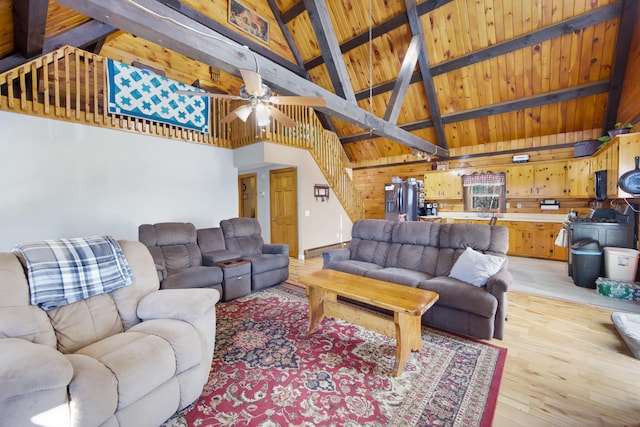 living room with high vaulted ceiling, wooden walls, beamed ceiling, ceiling fan, and light hardwood / wood-style flooring