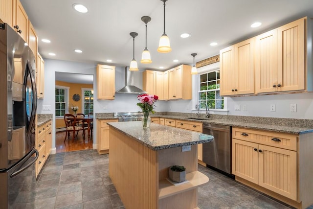 kitchen featuring stainless steel appliances, wall chimney range hood, pendant lighting, light brown cabinetry, and a kitchen island