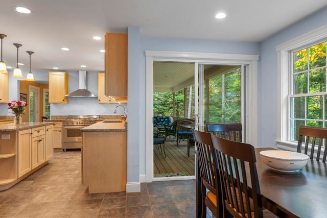 kitchen featuring light stone countertops, light brown cabinetry, pendant lighting, and wall chimney exhaust hood