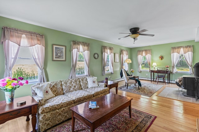 living room with ceiling fan, a wood stove, a healthy amount of sunlight, and light hardwood / wood-style flooring