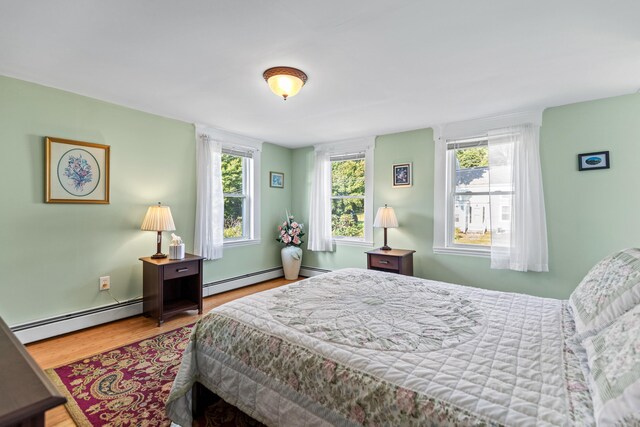 bedroom with multiple windows, hardwood / wood-style floors, and a baseboard radiator