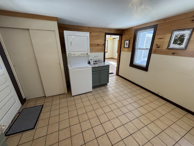 washroom with light tile patterned floors, cabinets, stacked washer / drying machine, and wood walls