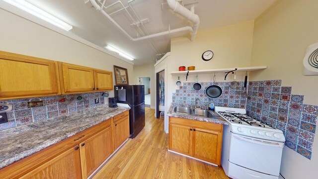 kitchen featuring decorative backsplash, light hardwood / wood-style floors, white gas range oven, sink, and black fridge