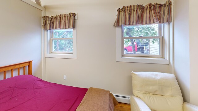 bedroom with multiple windows, hardwood / wood-style floors, and baseboard heating