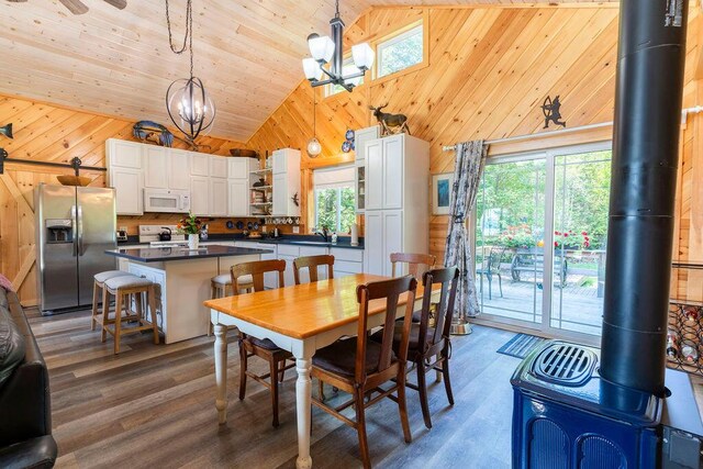 dining room with an inviting chandelier, wooden walls, a wood stove, and a healthy amount of sunlight