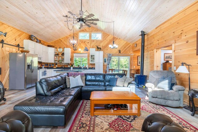 living room with a wood stove, wooden walls, high vaulted ceiling, an inviting chandelier, and a barn door