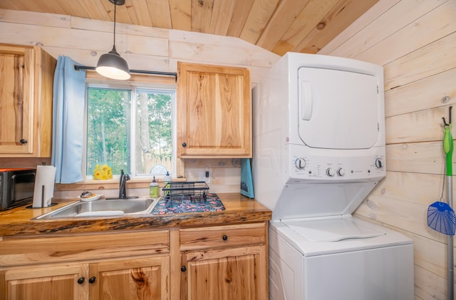 laundry area with wood ceiling, wooden walls, stacked washer and dryer, and sink