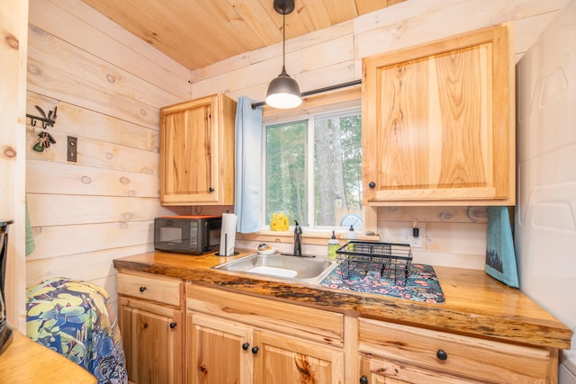 kitchen featuring light brown cabinetry, wooden walls, decorative light fixtures, and sink