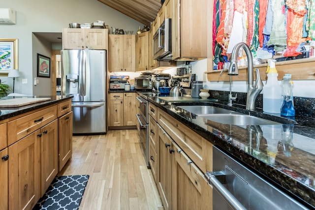 kitchen with dark stone counters, light hardwood / wood-style floors, sink, lofted ceiling, and stainless steel appliances