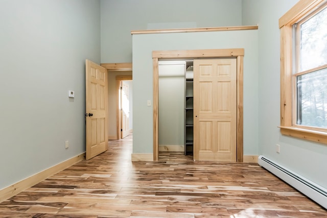 unfurnished bedroom featuring light hardwood / wood-style floors, a baseboard heating unit, and a closet