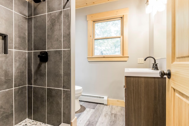 bathroom with vanity, baseboard heating, a tile shower, toilet, and hardwood / wood-style floors