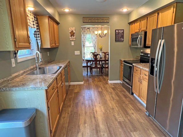 kitchen with sink, a chandelier, hardwood / wood-style flooring, stainless steel appliances, and light stone countertops