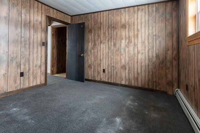 carpeted spare room with wood walls and baseboard heating