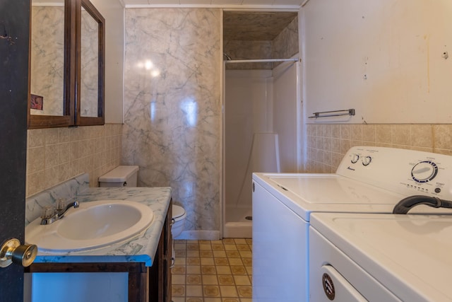 interior space with tile walls, a shower, vanity, toilet, and washer and dryer