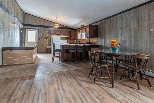 dining space featuring wooden walls, light wood-type flooring, vaulted ceiling, and a textured ceiling