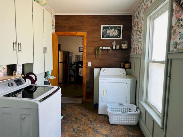 laundry area with a healthy amount of sunlight, washing machine and dryer, wooden walls, and cabinets