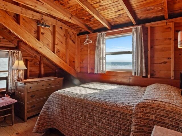 bedroom featuring wooden walls, hardwood / wood-style floors, a water view, and wooden ceiling