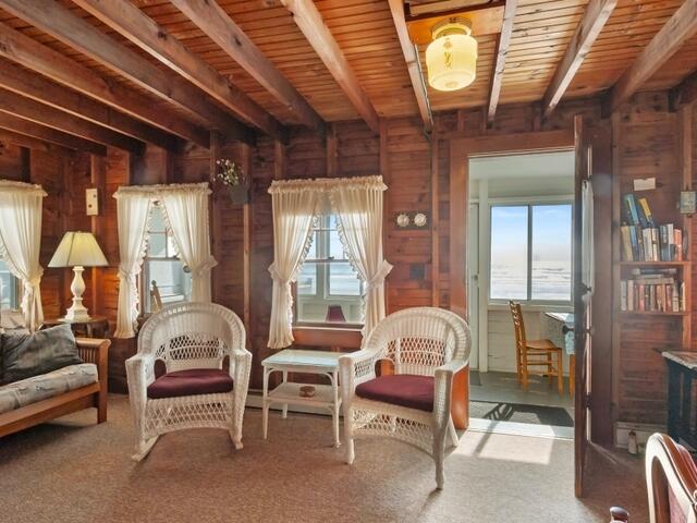 sitting room with beam ceiling, wood walls, wooden ceiling, and carpet floors