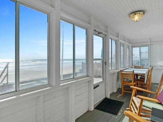 sunroom / solarium featuring a beach view, plenty of natural light, and a water view