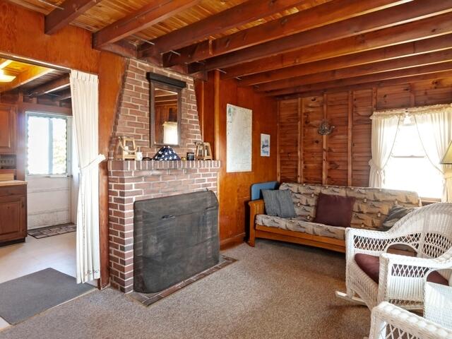 living room featuring wood ceiling, a brick fireplace, beam ceiling, and wood walls