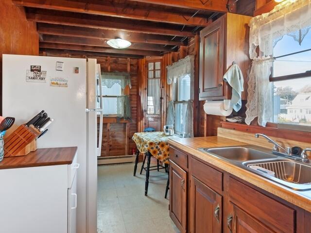 kitchen featuring white refrigerator, beam ceiling, sink, baseboard heating, and wood counters