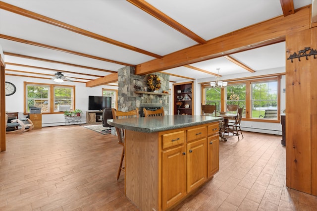 kitchen featuring a breakfast bar, ceiling fan with notable chandelier, a stone fireplace, beam ceiling, and a center island