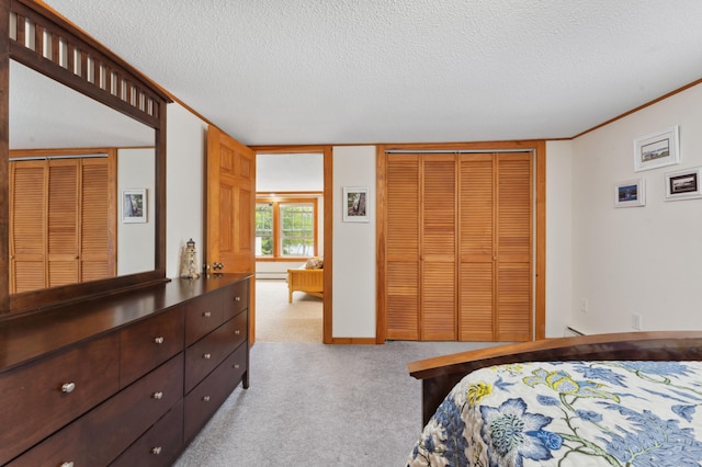 carpeted bedroom with a textured ceiling, ornamental molding, and multiple closets