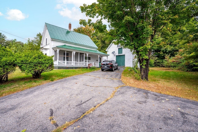 view of front of property with aphalt driveway, metal roof, a chimney, a front lawn, and a porch