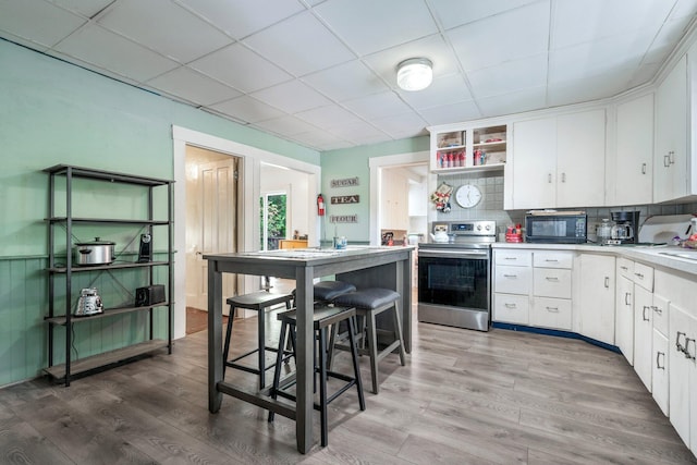 kitchen featuring light hardwood / wood-style floors, stainless steel electric range, white cabinets, backsplash, and a drop ceiling