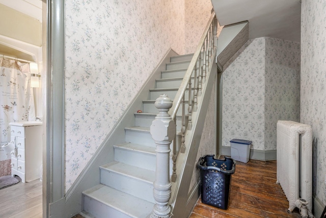 stairway with wallpapered walls, radiator, and wood finished floors