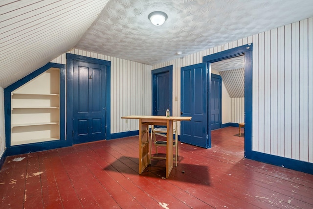 additional living space featuring built in shelves, lofted ceiling, and dark wood-type flooring