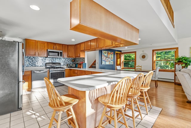 kitchen featuring stainless steel appliances, tasteful backsplash, kitchen peninsula, a breakfast bar area, and light wood-type flooring