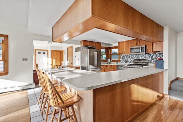 kitchen with light hardwood / wood-style floors, a kitchen bar, kitchen peninsula, and stainless steel appliances