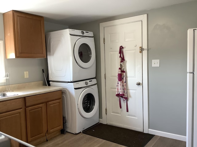 laundry room with cabinets, sink, stacked washing maching and dryer, and wood-type flooring