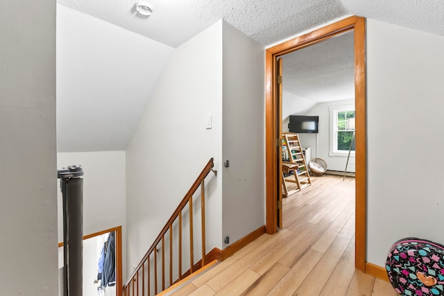 hall featuring light hardwood / wood-style flooring, vaulted ceiling, and a textured ceiling