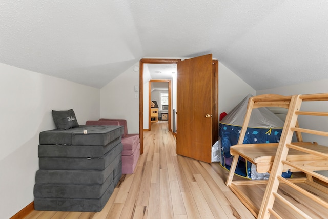 interior space featuring vaulted ceiling, light hardwood / wood-style floors, and a textured ceiling