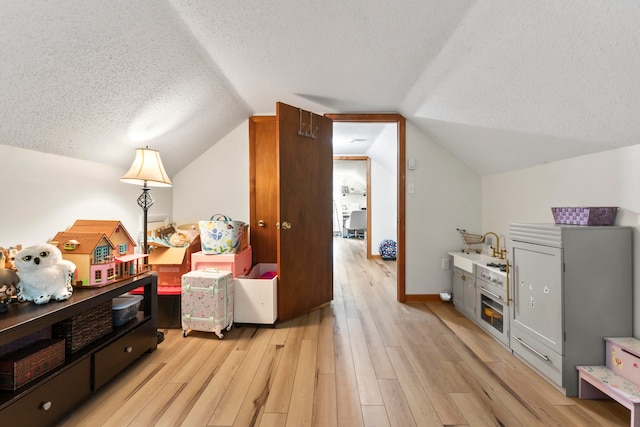 interior space with light wood-type flooring, vaulted ceiling, and a textured ceiling