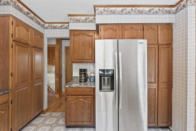 kitchen featuring stainless steel refrigerator with ice dispenser, a textured ceiling, light hardwood / wood-style floors, and crown molding