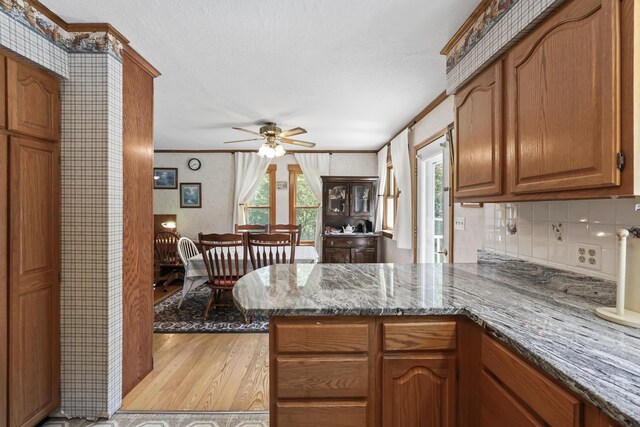 kitchen featuring kitchen peninsula, stone counters, ceiling fan, and light hardwood / wood-style flooring