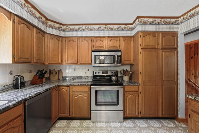 kitchen featuring appliances with stainless steel finishes, backsplash, dark stone countertops, and crown molding