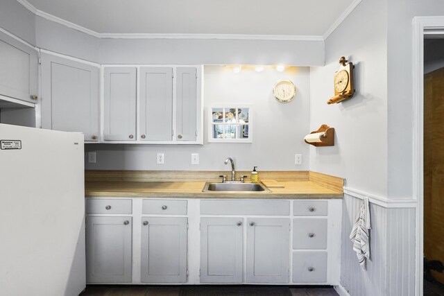 kitchen with ornamental molding, white cabinets, white refrigerator, and sink