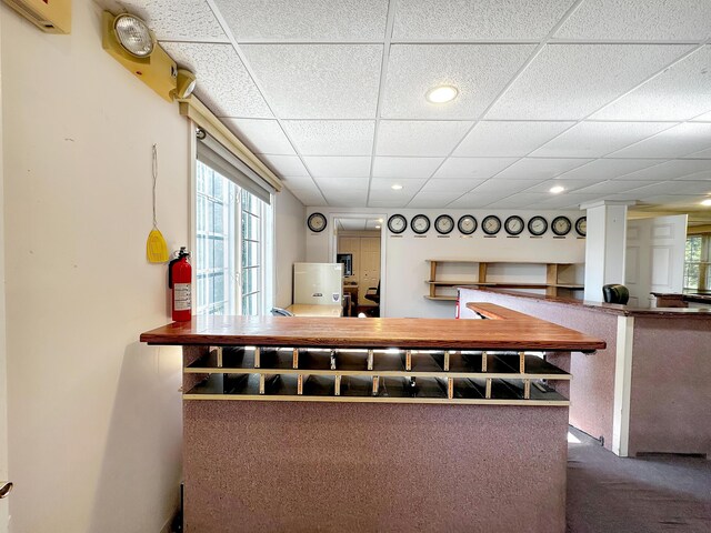 bar with a drop ceiling, dark carpet, and ornate columns